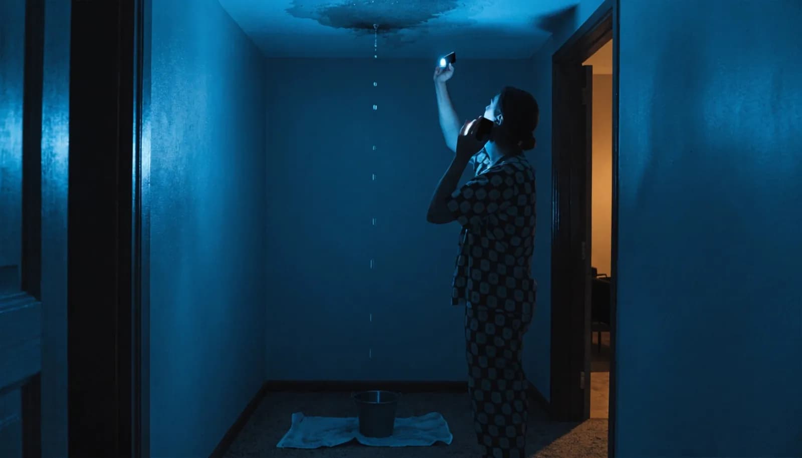 Homeowner calling an emergency plumber at night with water leaking from a ceiling